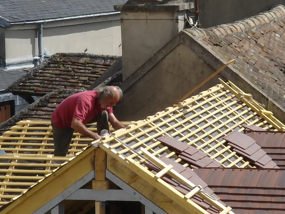 Couvreur posant des tuiles plates sur les liteaux d'une toiture neuve.